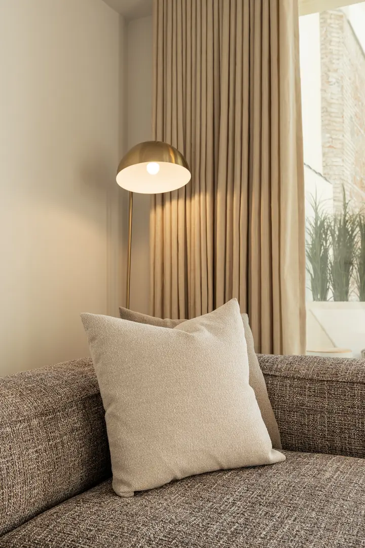 Close-up of a textured sofa with a cream cushion in the Toro residence, with a lit brass floor lamp