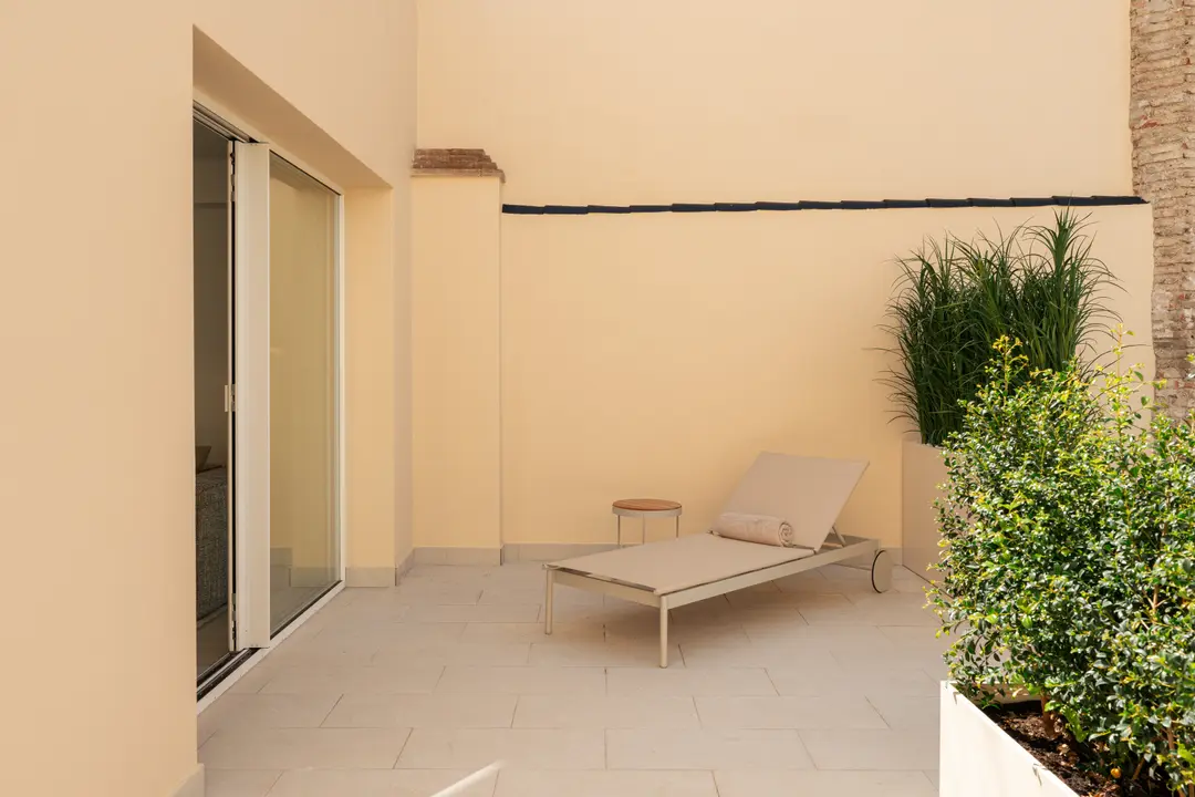 The private terrace of the Toro residence has a sun lounger, a small side table, and large planters with shrubs