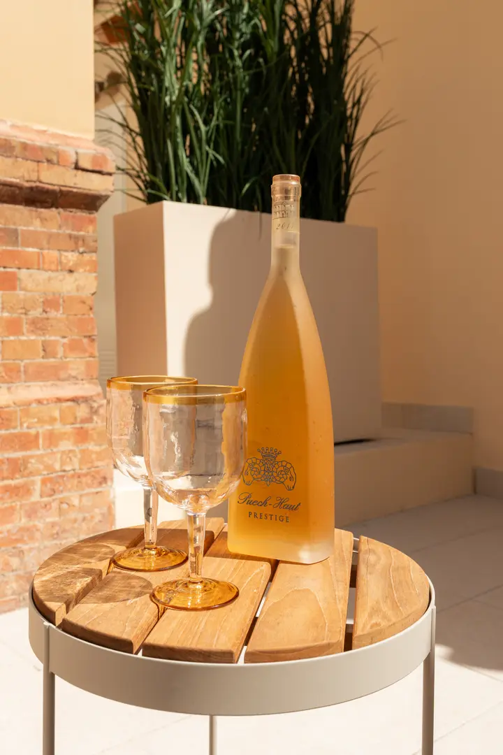 A bottle of rosé wine and two glasses on a wooden side table on the sunny terrace of the Toro residence