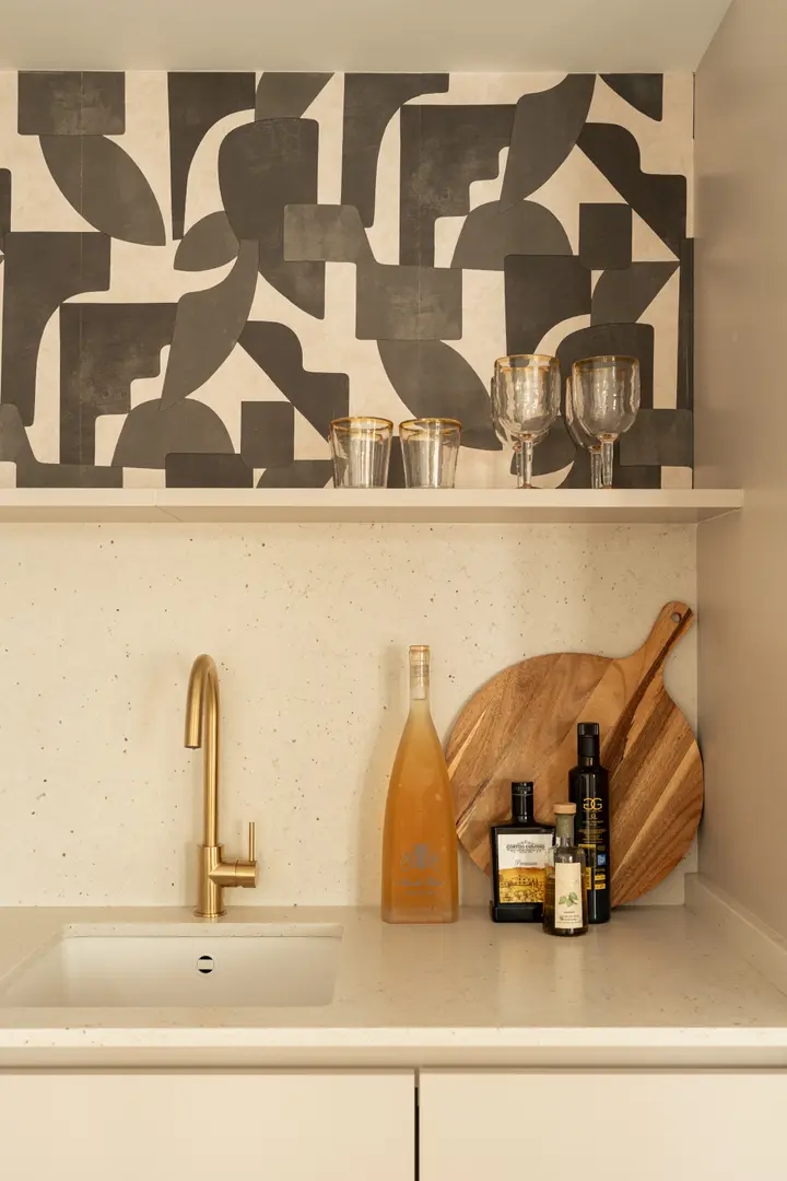 Detail of the Toro residence kitchen with a gold tap, terrazzo worktop, and a shelf against bold abstract wallpaper