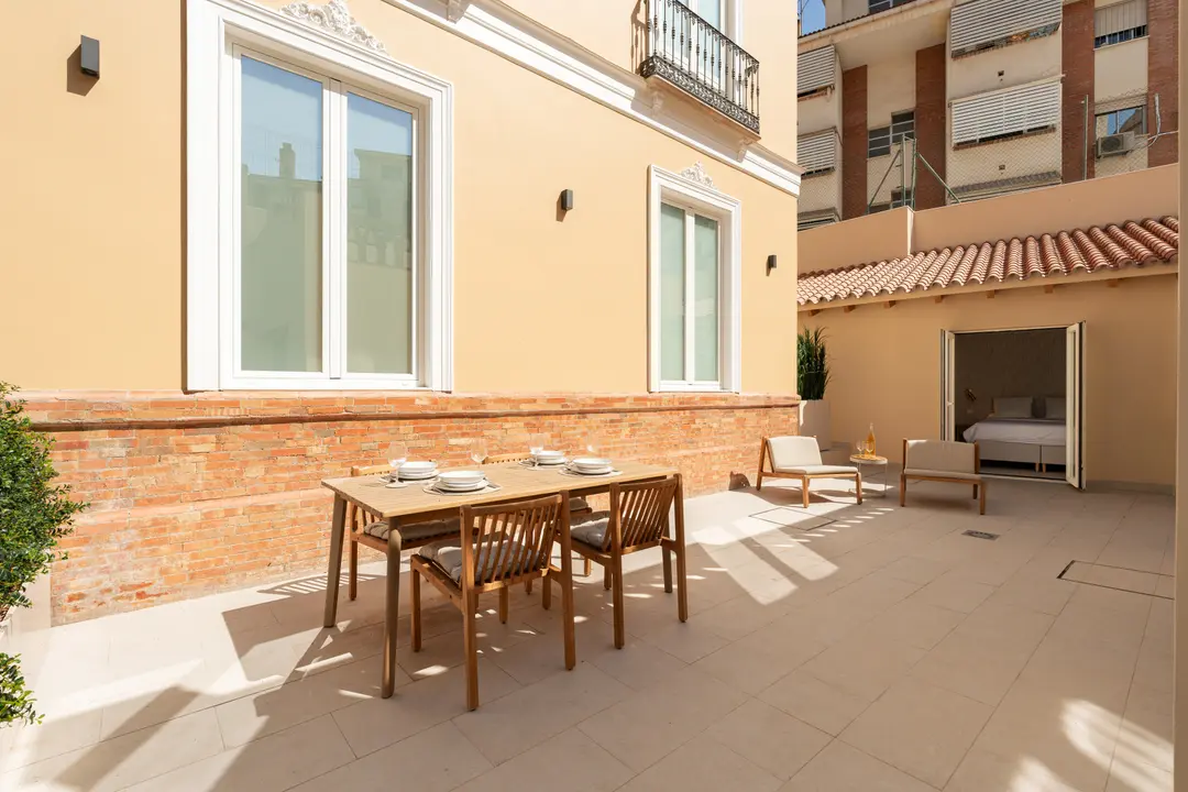 The sunny private patio of the Toro residence, with a wooden dining table and a seating area next to the bedroom entrance