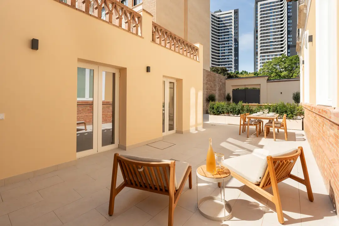 The sunny private terrace of the Toro residence, with wooden lounge chairs, a dining set, and a view of Málaga's modern towers