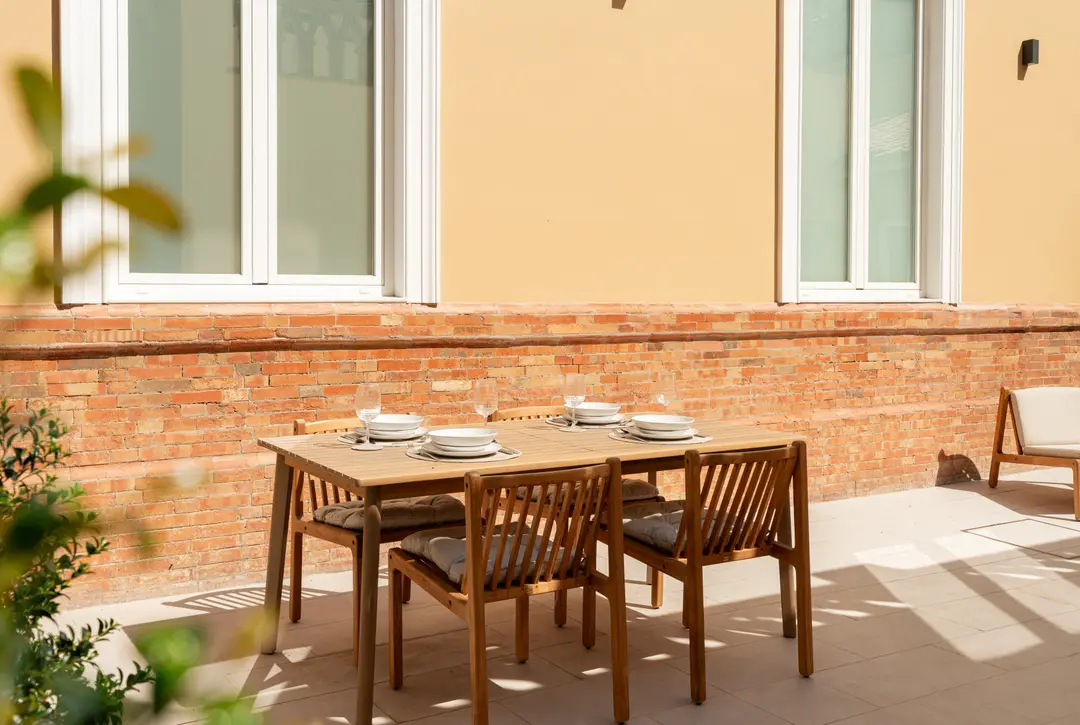 The sunny private terrace of the Toro residence, with a wooden dining table set for four against a red brick wall