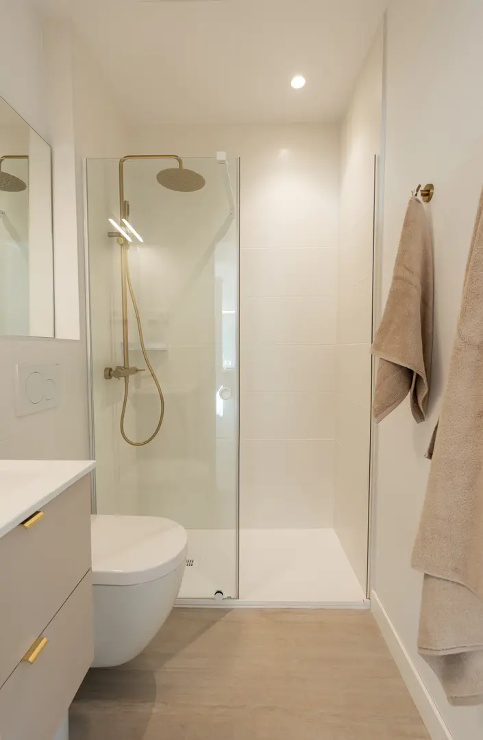 The bathroom in the Toro residence, with a walk-in shower featuring brushed gold fittings, a wall-hung toilet and a vanity unit
