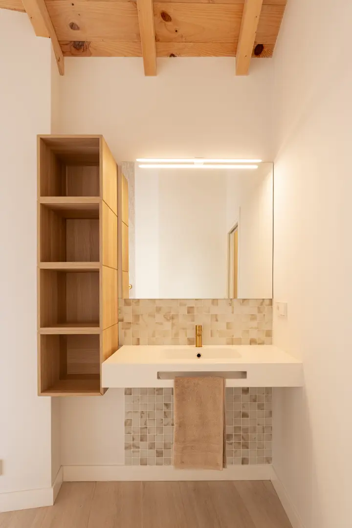 The Toro residence bathroom with a floating washbasin, gold tap, mosaic tiles, and open wooden shelving under an exposed beam ceiling