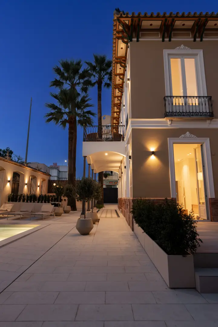 The stone-paved courtyard and facade of Palacete 10 at dusk, with warm lights illuminating the walkway and palm trees