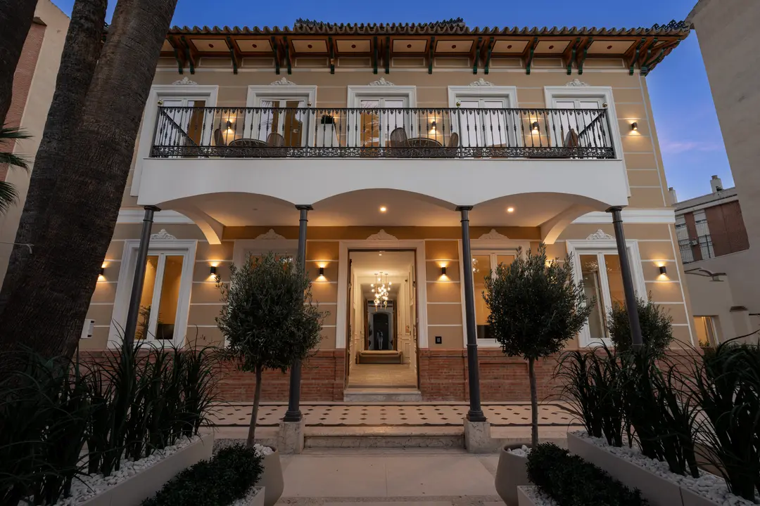 The restored facade of Palacete 10 in Málaga, lit up at dusk, with its grand entrance and first-floor balcony