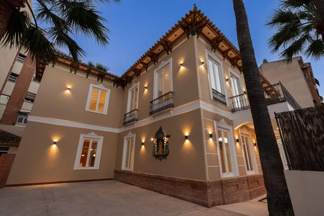 The restored Palacete 10 villa at dusk, its warm beige facade illuminated by wall lights under a deep blue sky