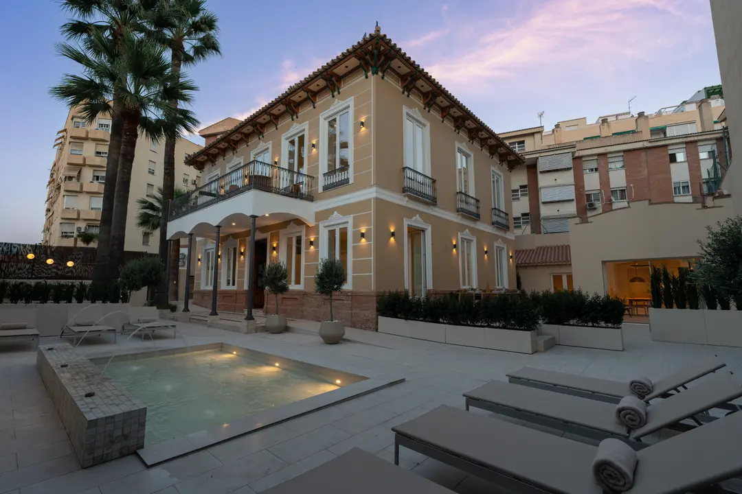 The restored villa of Palacete 10 seen from its courtyard at dusk, with the illuminated pond and sun loungers