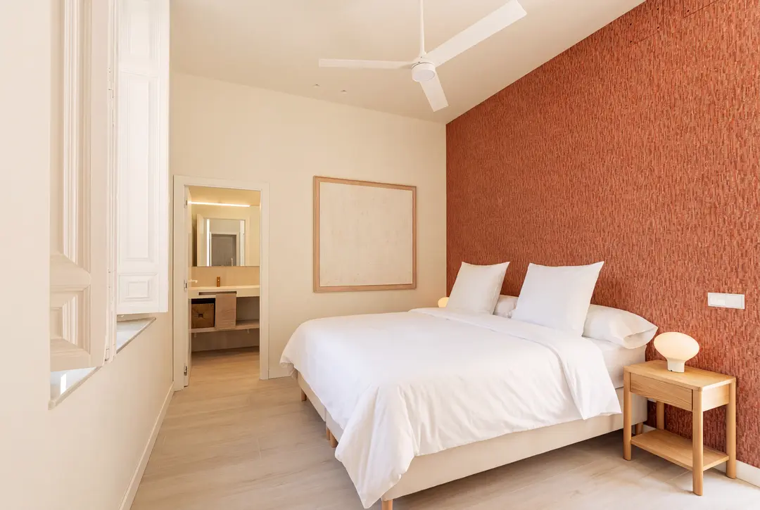 The bedroom in the Vino residence has a textured terracotta feature wall behind the double bed, with the ensuite bathroom visible