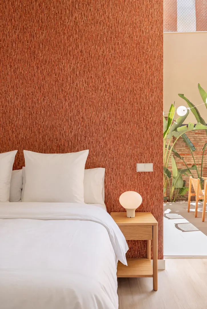 Bedroom in the Vino residence with a terracotta textured wall, white bedding, and an oak bedside table looking onto a sunny private terrace