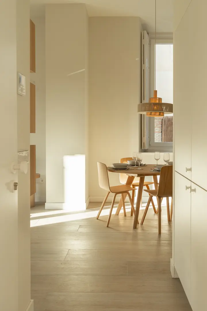 The dining area in the Vino residence, with a round wooden table and chairs lit by warm afternoon sunlight