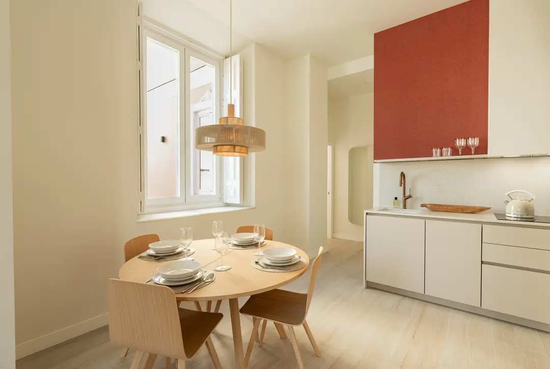 The Vino residence's open-plan dining area with a round wooden table and an adjoining kitchen with a wine-red feature wall