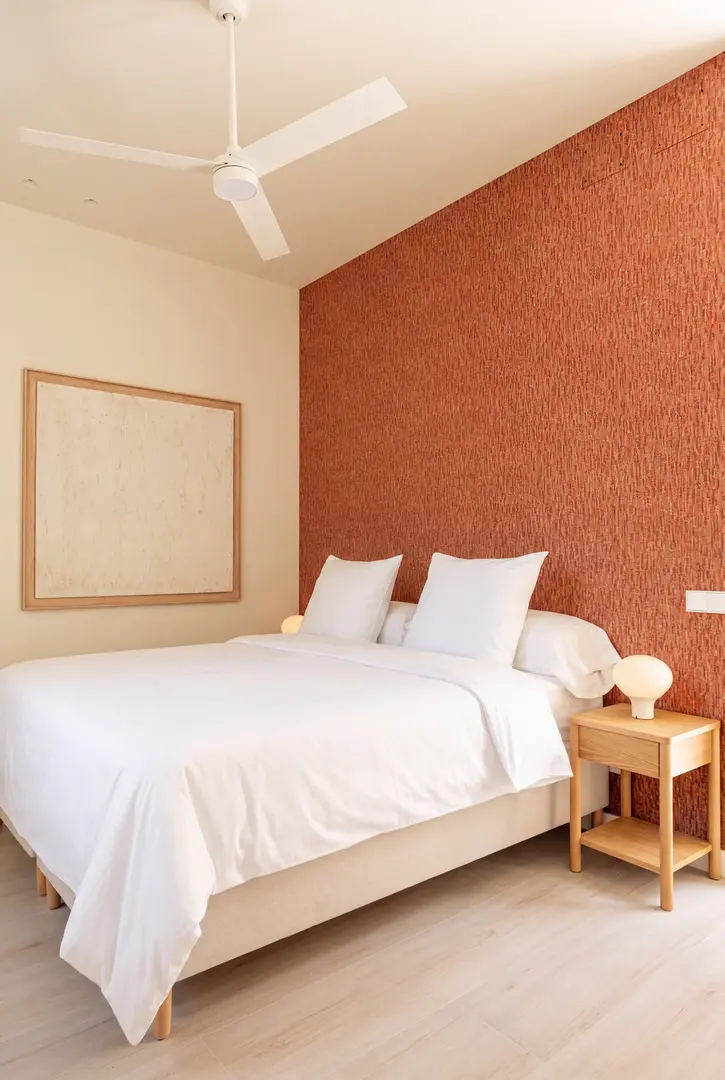 The bedroom in the Vino residence, with a double bed and a terracotta-coloured cork feature wall. The bed has a white waffle bedspread, and the floor is light wood-effect
