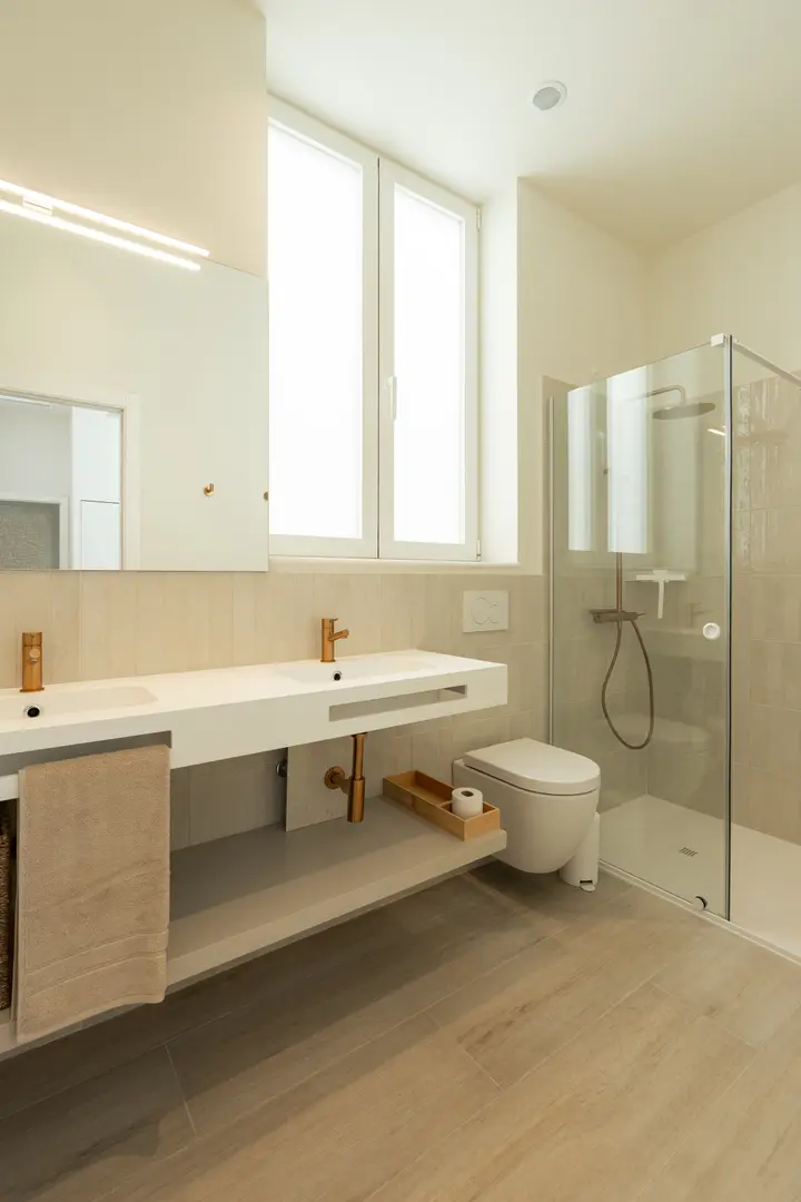 Brightly lit bathroom in the Vino residence with a double vanity, walk-in rain shower, and bronze-coloured taps on wood-effect flooring