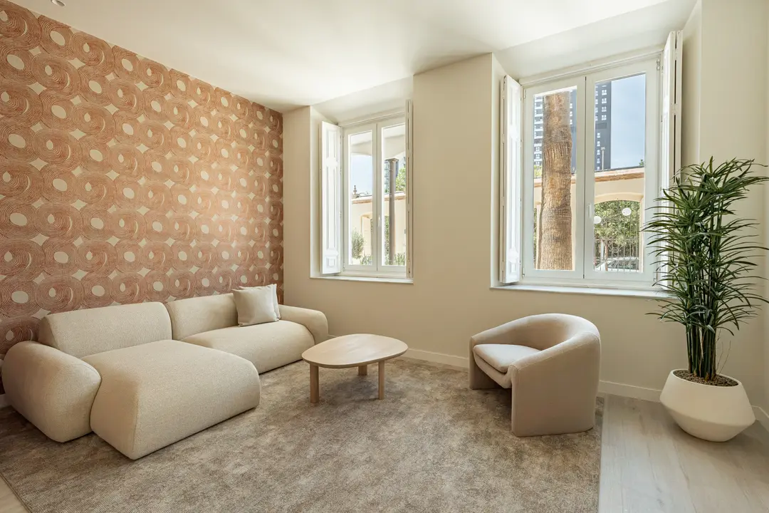 Living room in the Vino residence with a cream bouclé sofa and armchair, and a feature wall with terracotta patterned wallpaper