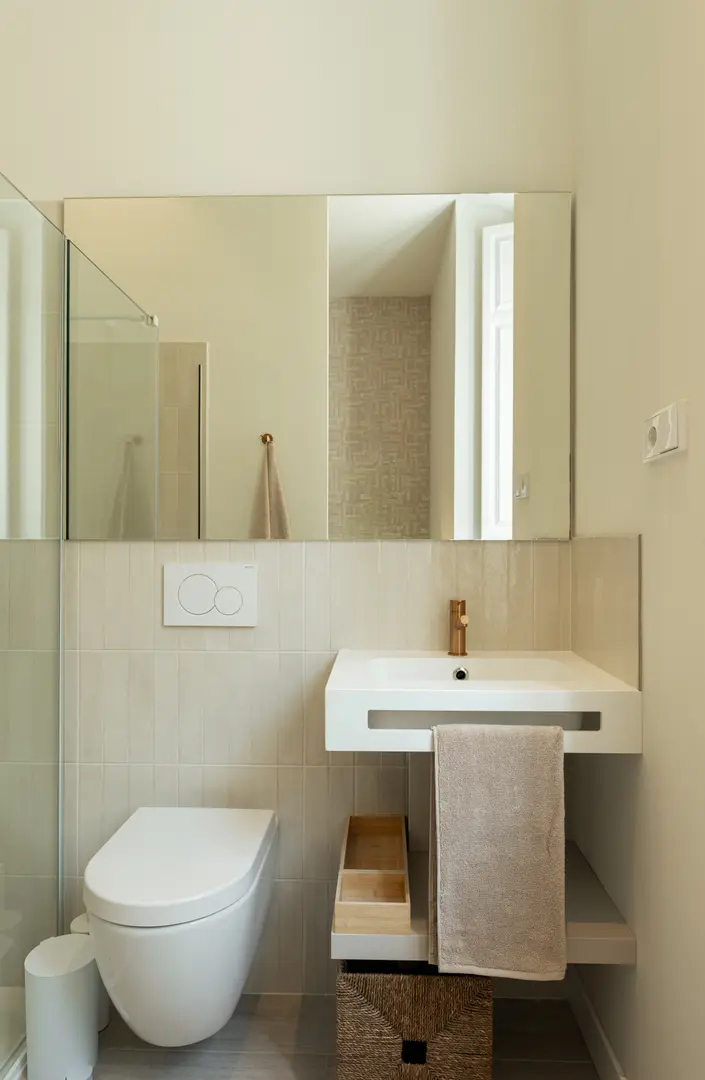 The modern bathroom in the Vino residence, with a wall-hung toilet, a white sink with a copper tap, and beige tiles