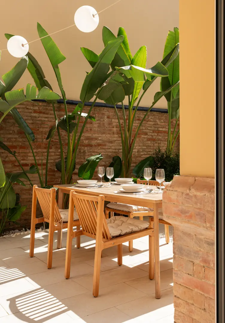 The sunny private patio of the Vino residence, with a wooden dining table set for a meal beside lush plants