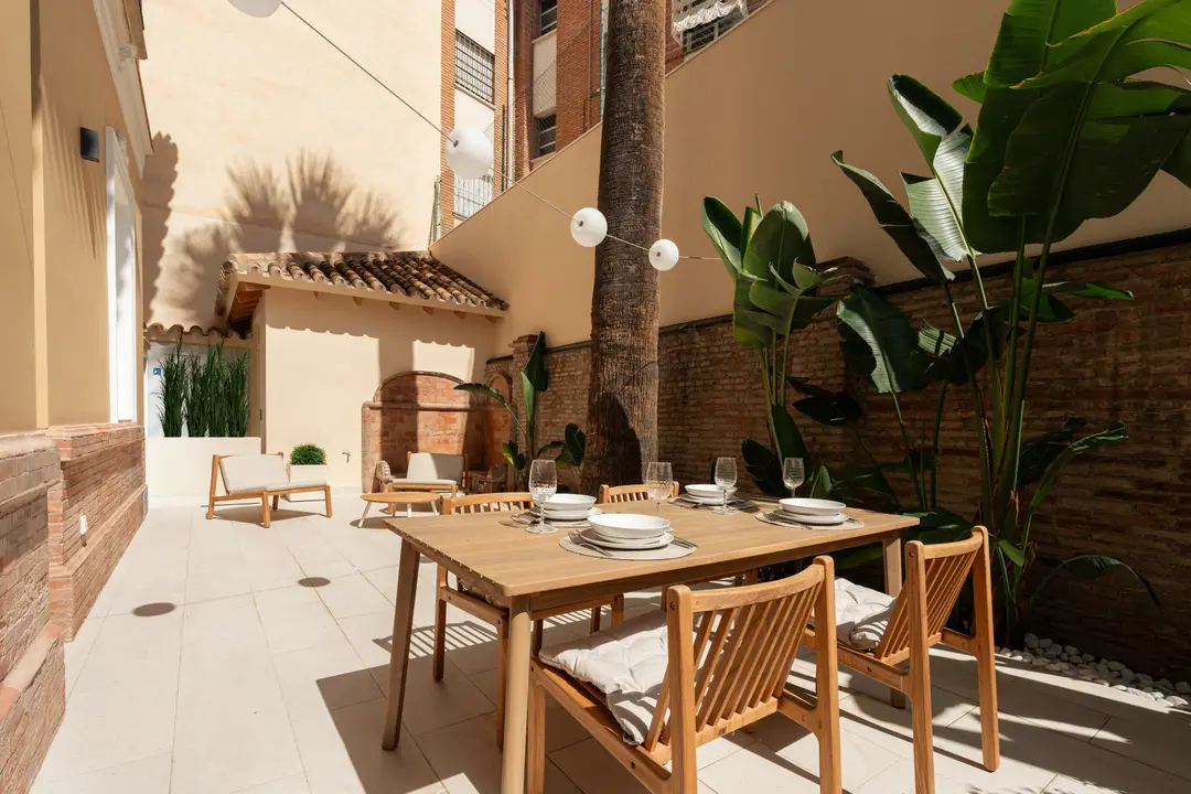 The sunny private patio of the Vino residence, with a wooden dining table set for six beside a palm tree