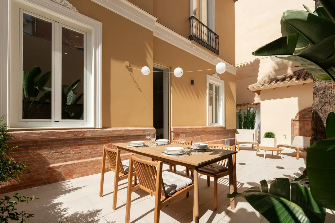 The sunny private terrace of the Vino residence, with a wooden dining table set for four against an ochre wall