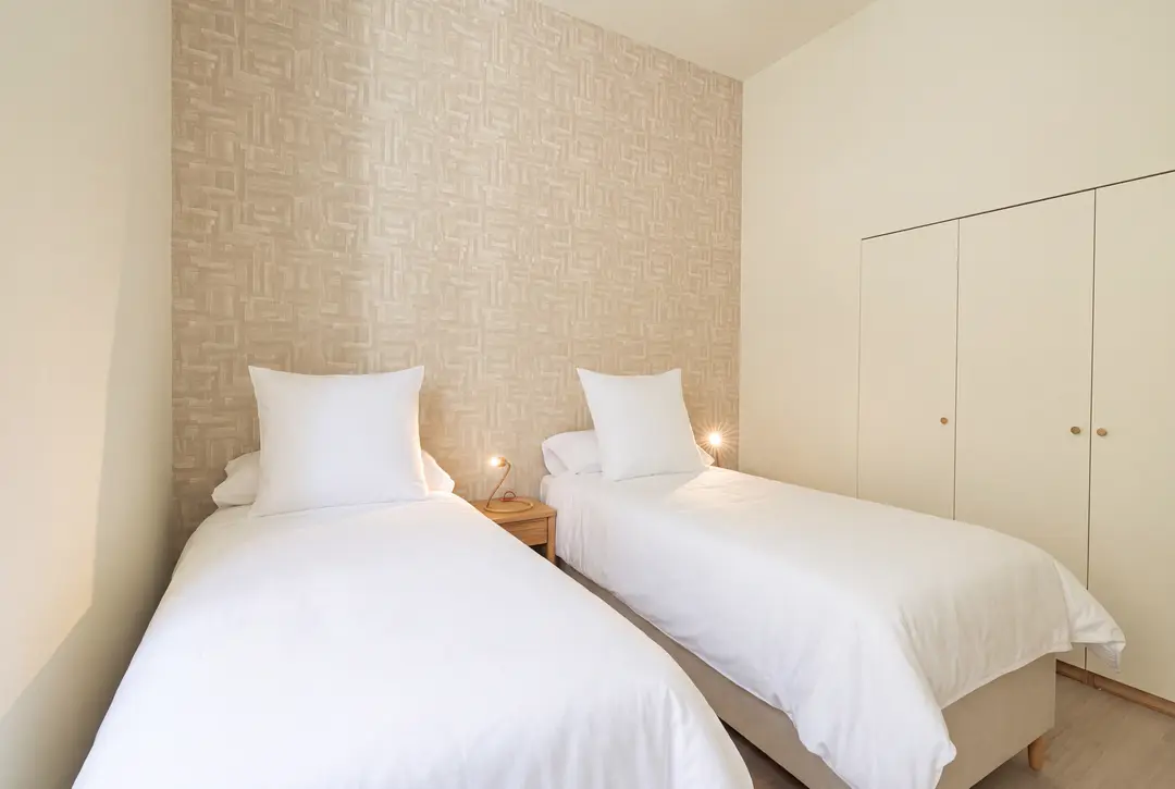 The twin bedroom in the Vino residence, with two single beds, textured wallpaper, and built-in wardrobes with brass handles