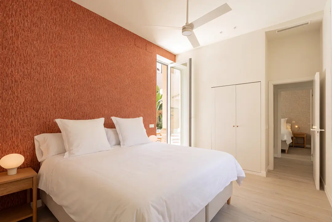 The main bedroom in the Vino residence, with a textured terracotta wall, a double bed, and doors to a terrace and a second bedroom