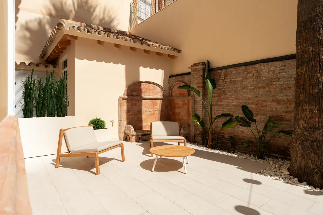 The sunny private patio of the Vino residence, with two wooden armchairs and a coffee table on pale stone tiles