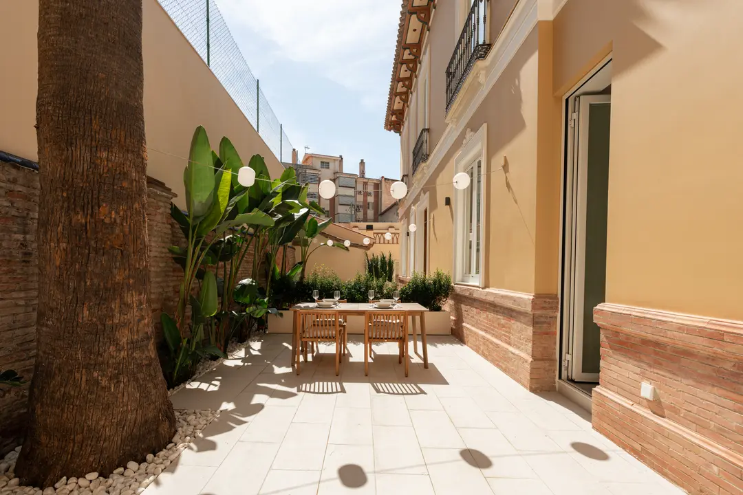 The sunny private terrace of the Vino residence, with a wooden dining table set for four next to a palm tree