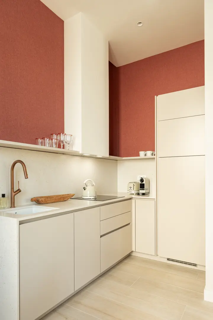 The modern kitchen in the Vino residence features cream units, a copper tap, and striking deep red textured walls