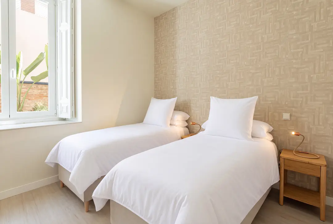The twin bedroom in the Vino residence, with two single beds, patterned wallpaper, and a window overlooking a private patio