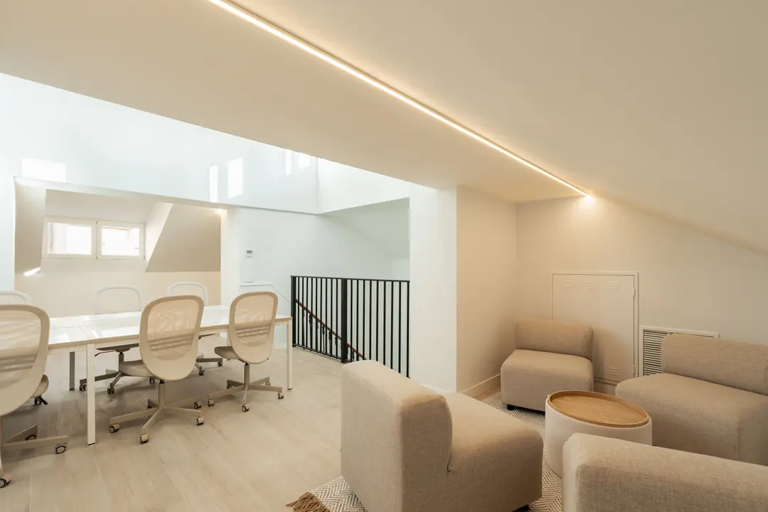 The bright attic work suite at Palacete 10, with a long shared table and a separate lounge area with armchairs