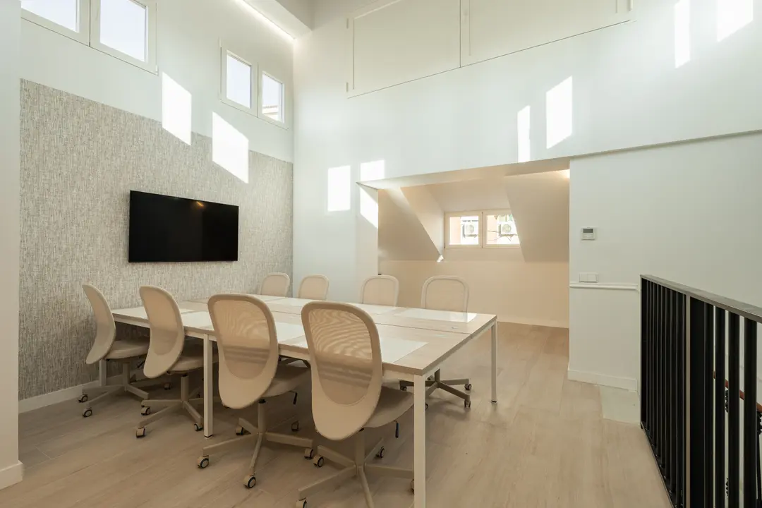 The bright attic work suite with a long table for eight, a large screen, and sunlight from high windows