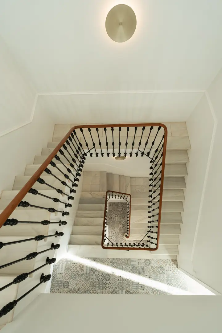 Looking down the main staircase at Palacete 10, with its marble steps, iron balustrade, and sunlit tiled landing