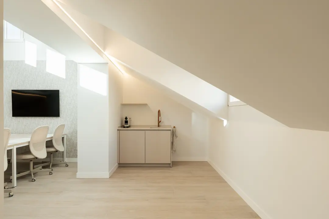 The bright attic work suite with light wood floors, showing the kitchenette and part of the large shared table and screen