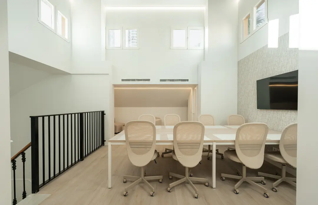 The bright, double-height work suite at Palacete 10, with a long shared table, mesh office chairs, and light wood floors